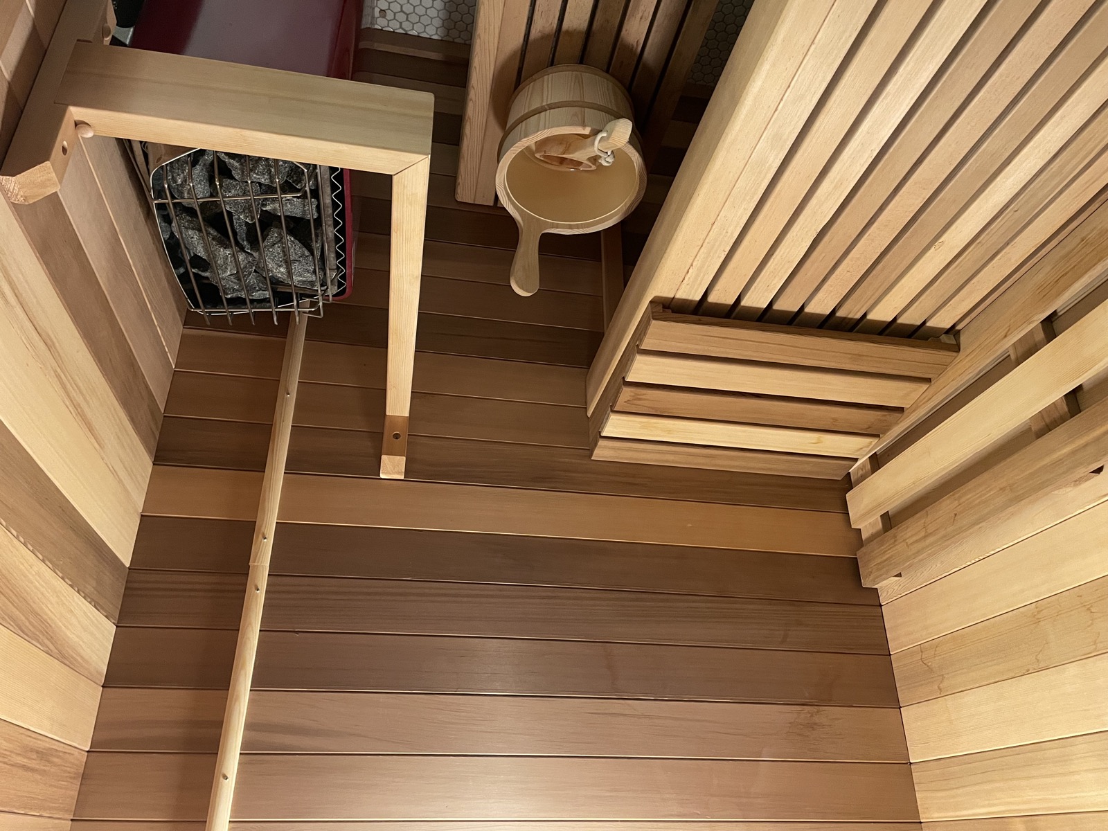 Finnish sauna interior showing cedar benches, heater with stones, and wooden bucket